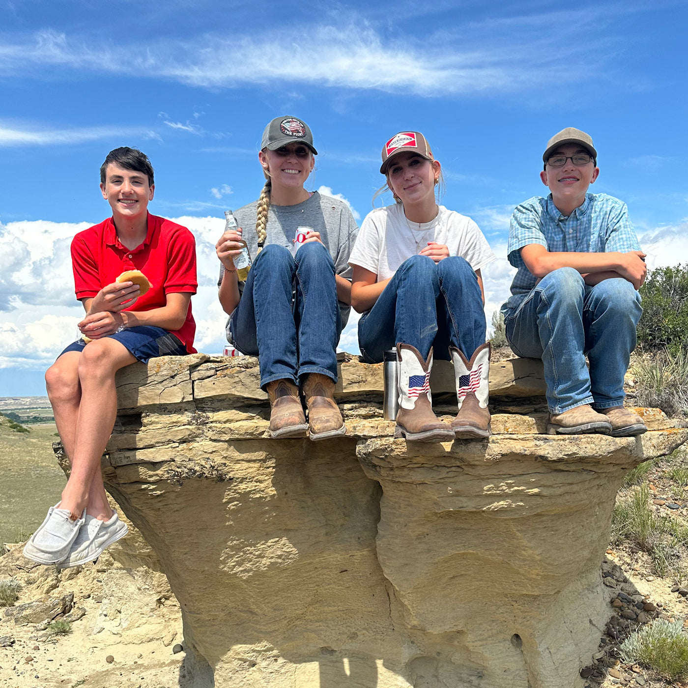 Four young people sitting on a rocky outcrop with a clear blue sky in the background.