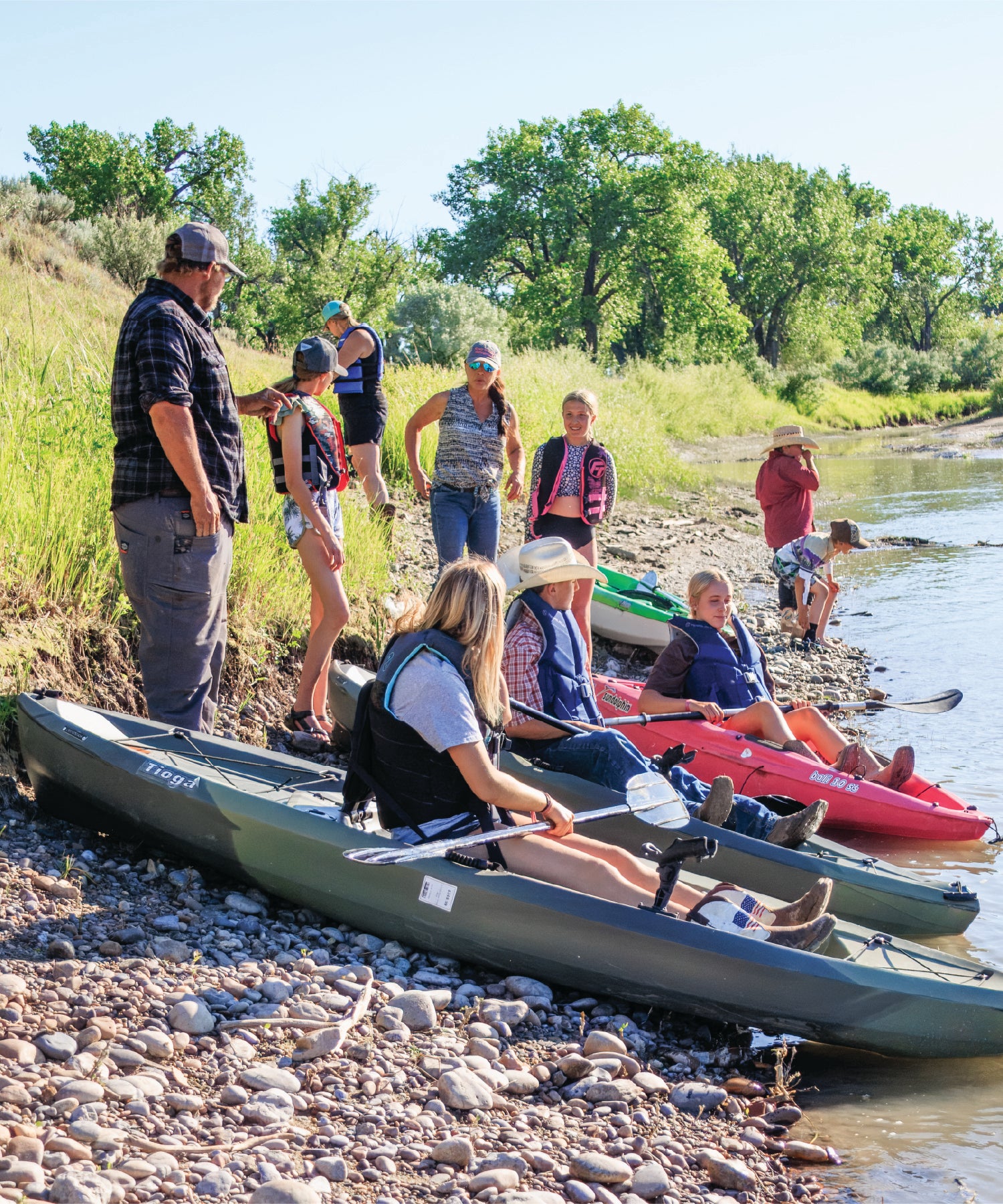 Group of people preparing to kayak on the Yellowstone River with kayaks on the shore.