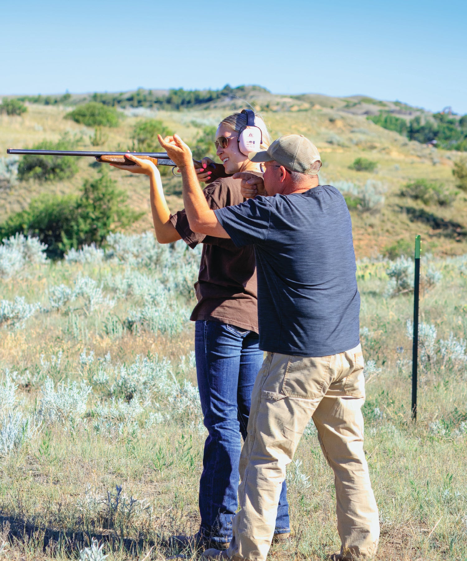 Two people in a field with one holding a shotgun