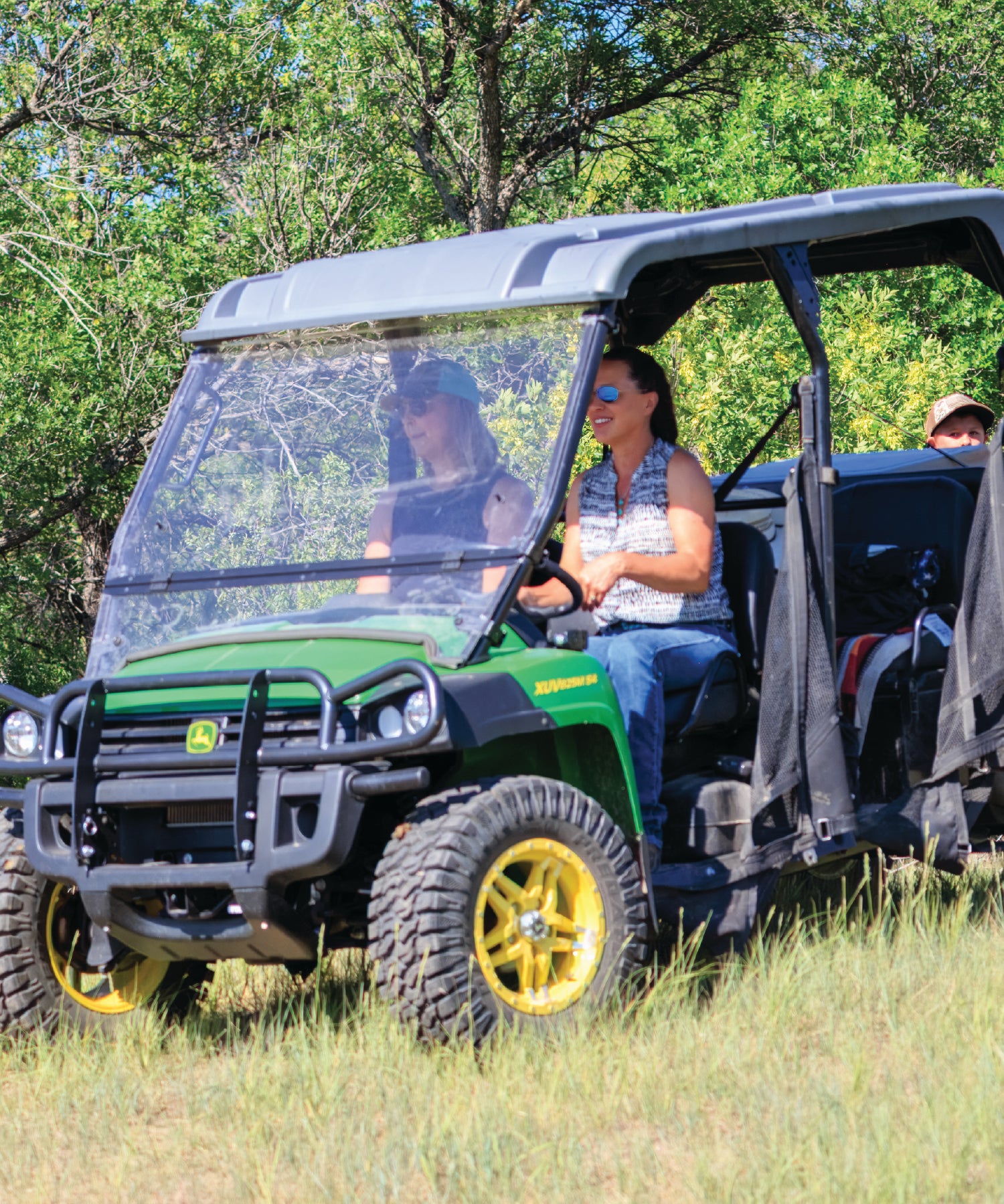 Green and black off-road vehicle with people inside on a grassy area with trees in the background