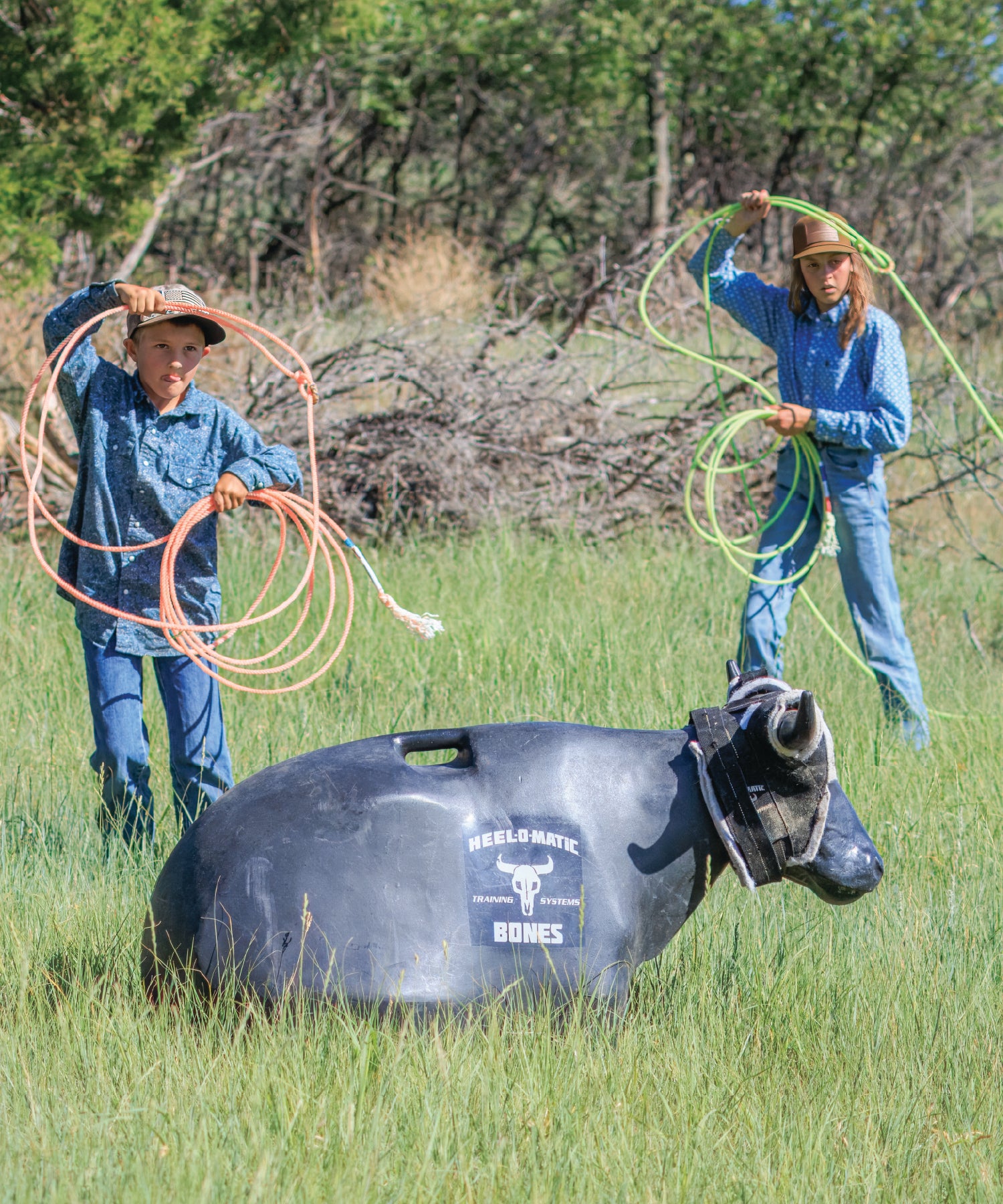 Two children with lassos and a model steer target in a grassy field.