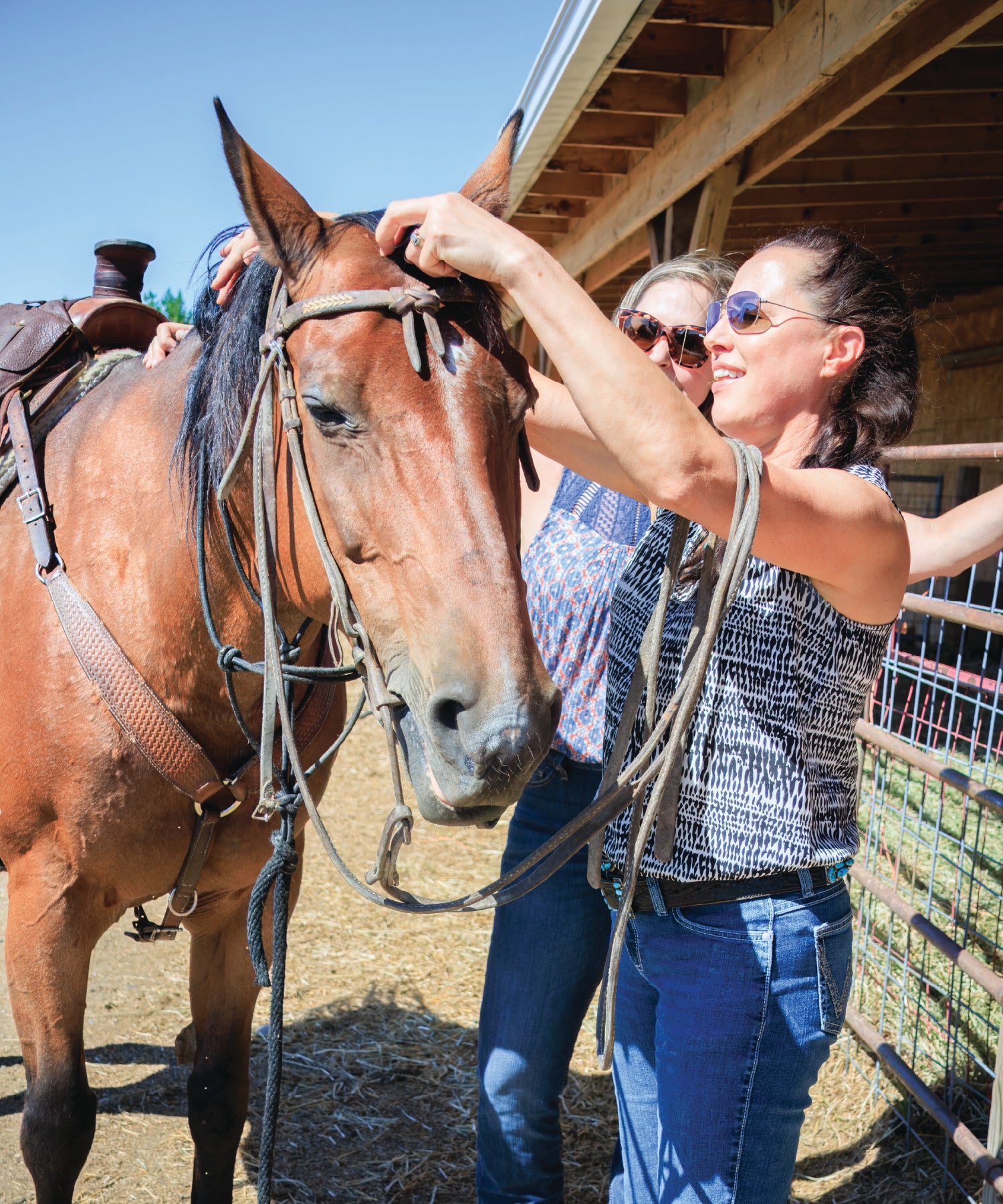 Two women interacting with a horse near a stable