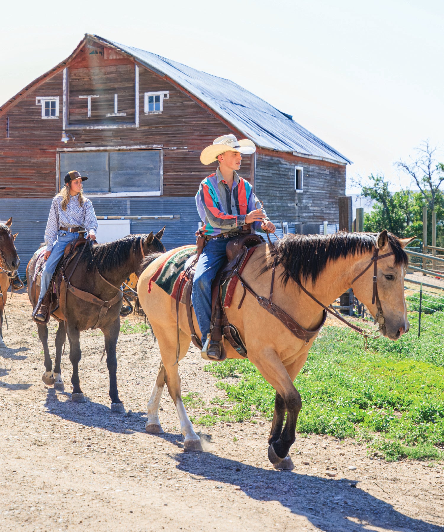 Two people riding horses with a barn in the background