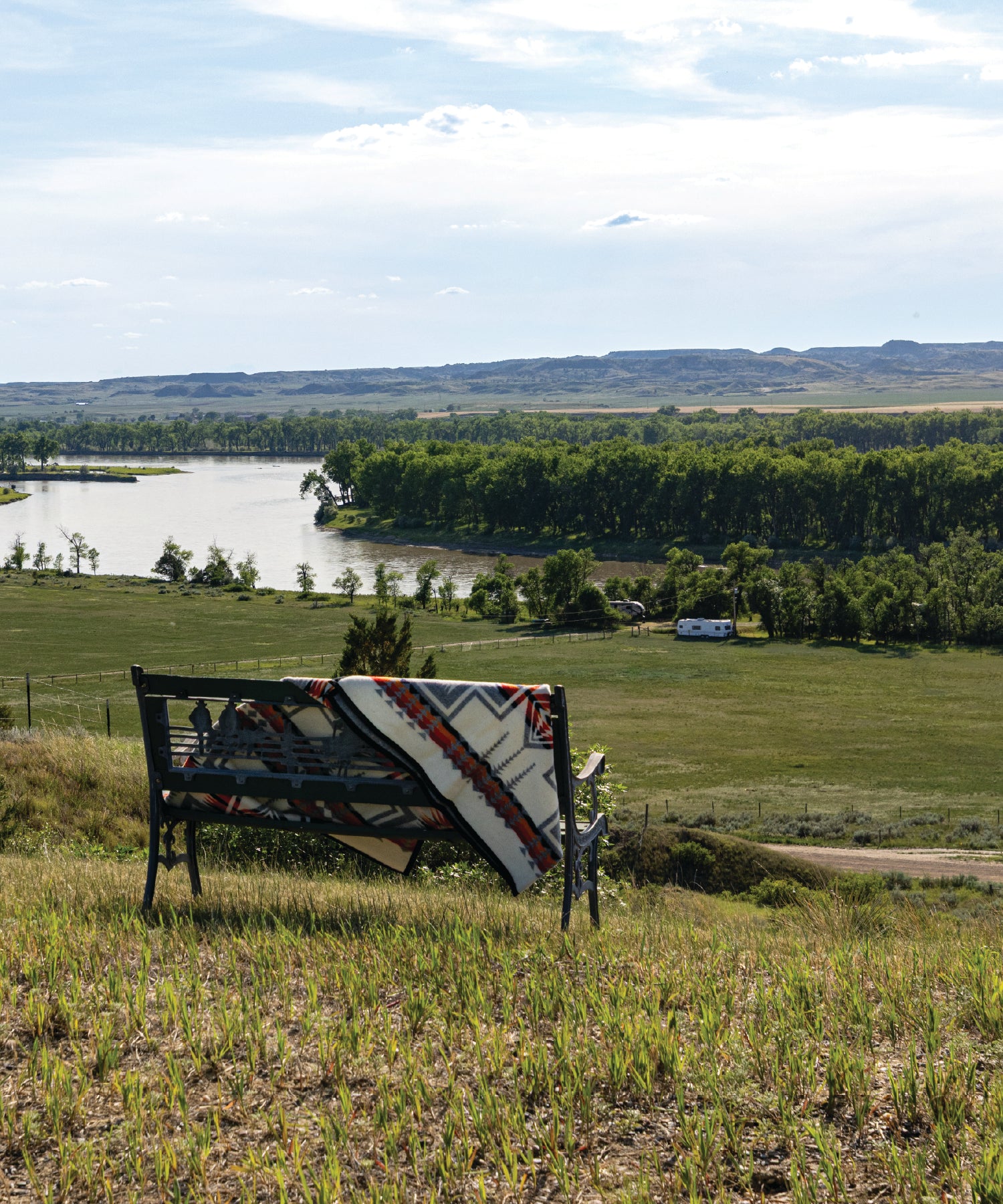 Bench with a patterned blanket in a scenic landscape with the Yellowstone River and hills.