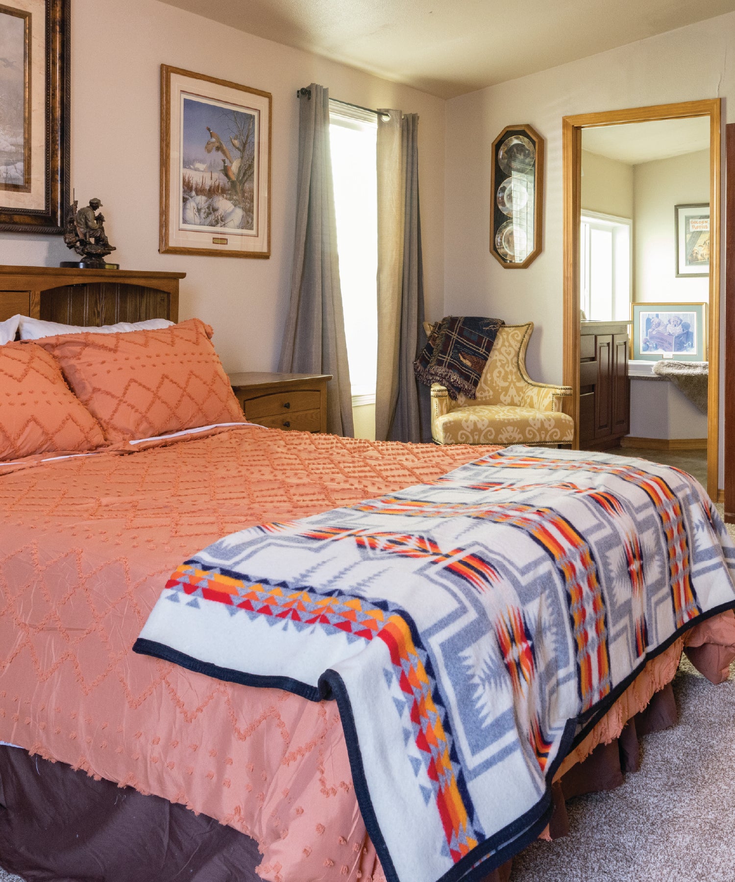 Montana bedroom with a bed featuring a colorful quilt, framed pictures on the wall, and a chair.