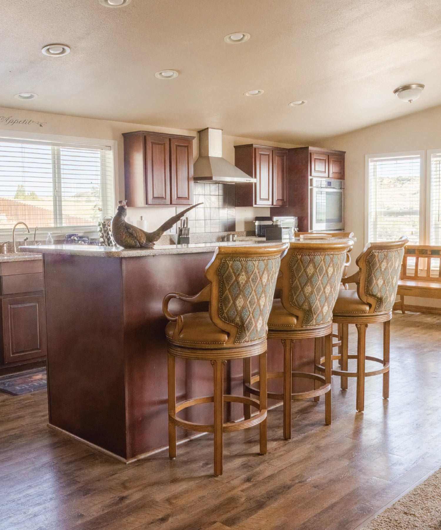 Kitchen with wooden island and bar stools, featuring a stove and sink with pheasant decor