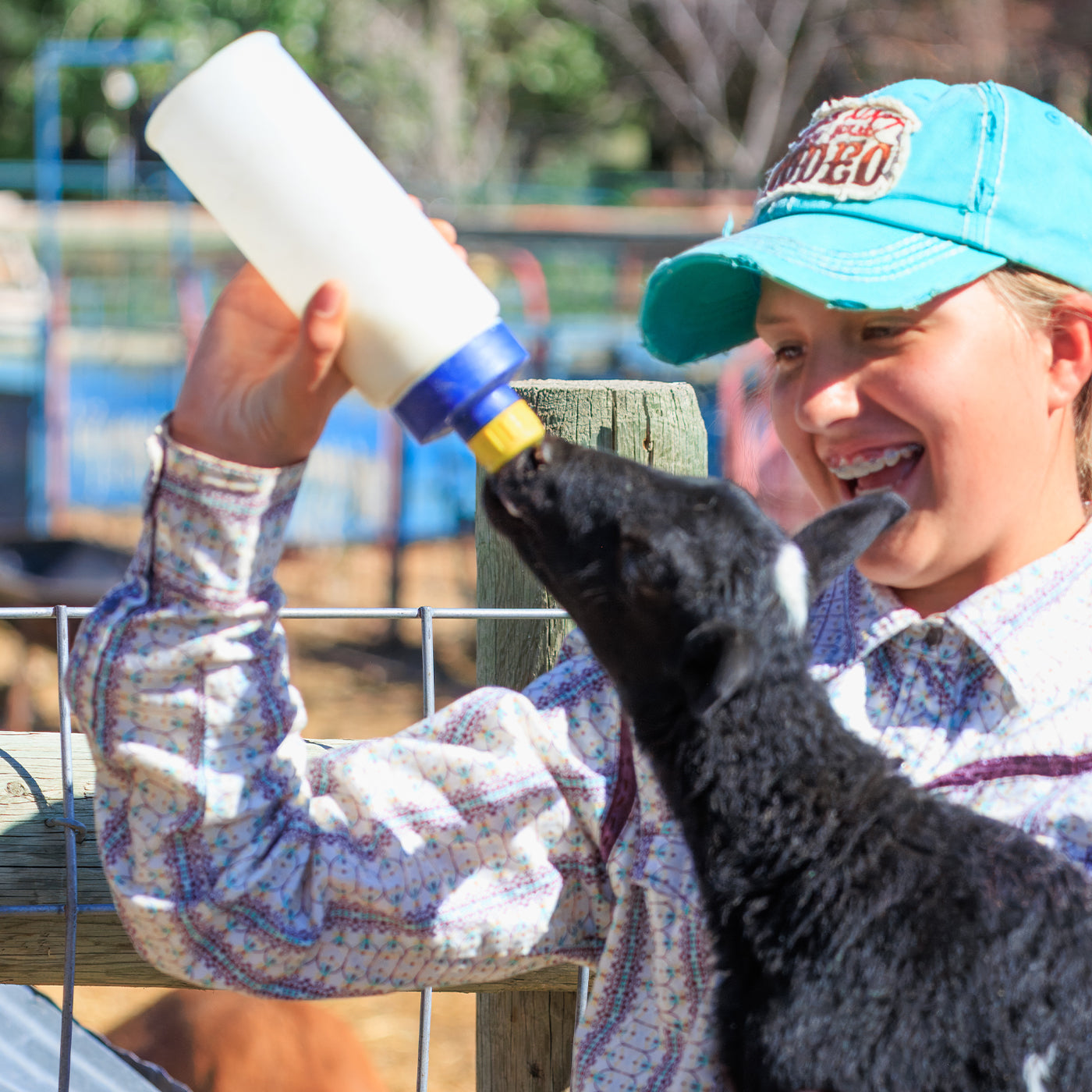 Teen feeding a lamb with a bottle in an outdoor setting while smiling