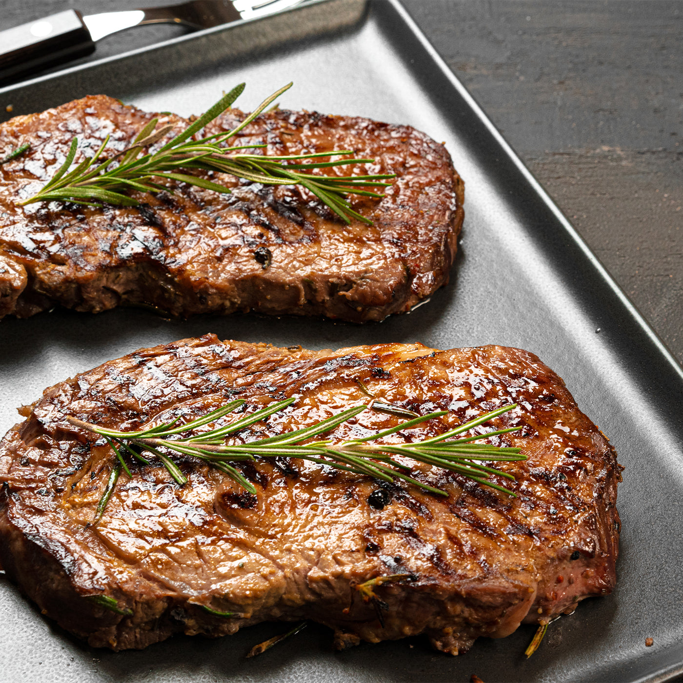 Two grilled steaks with rosemary on a silver tray